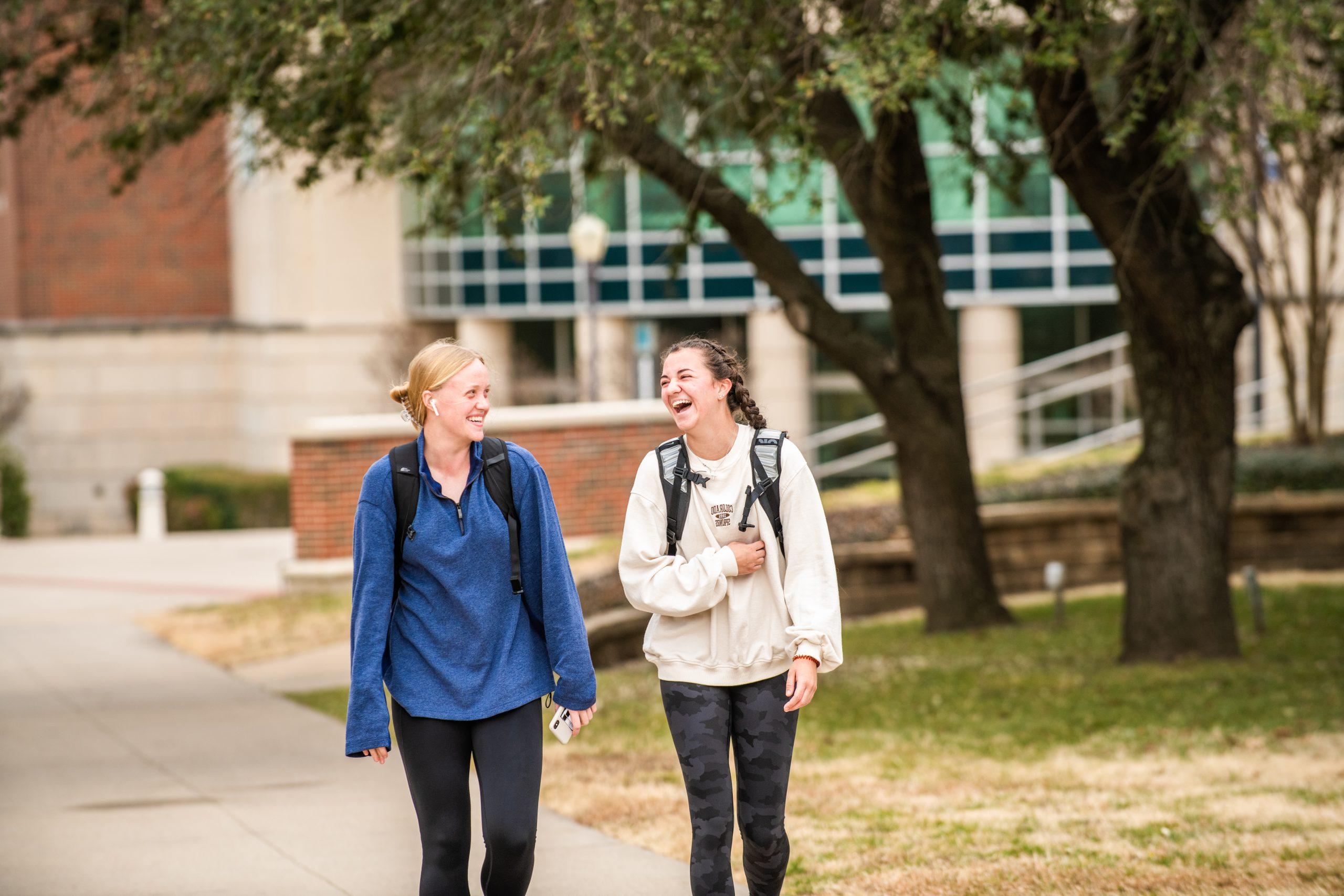 Two female students walking and speaking outside.